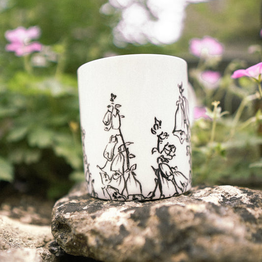 White mug with black illustrations on stone with greenery in the background.