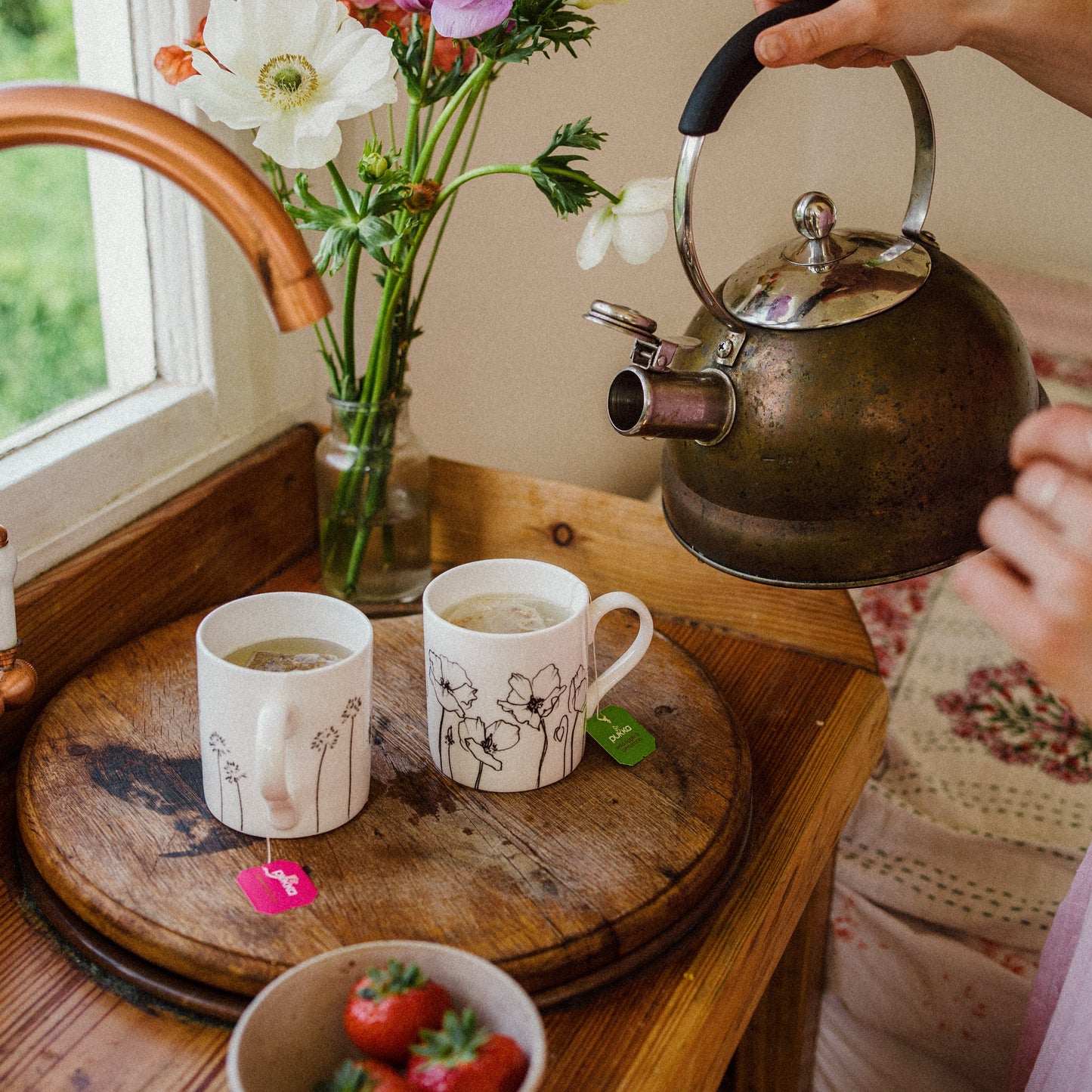 Two white mugs on a wooden surface with a kettle