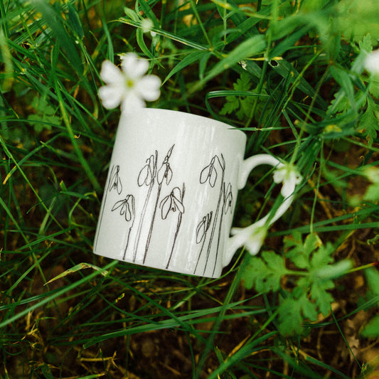 White mug with line drawings of flowers, laid on grassy background