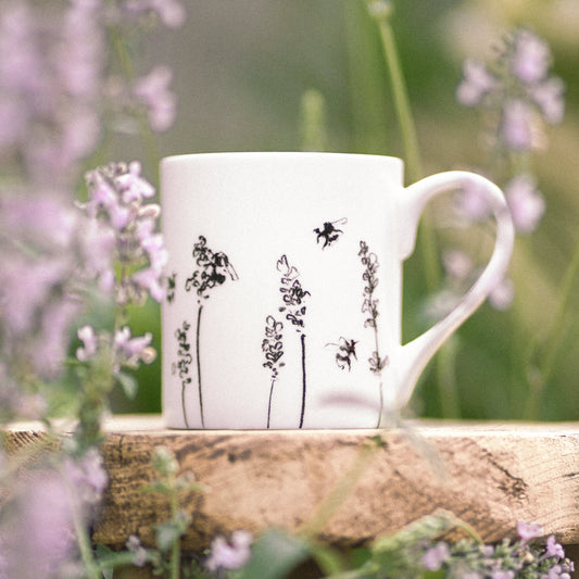 White mug with black floral design on a wooden surface surrounded by purple flowers