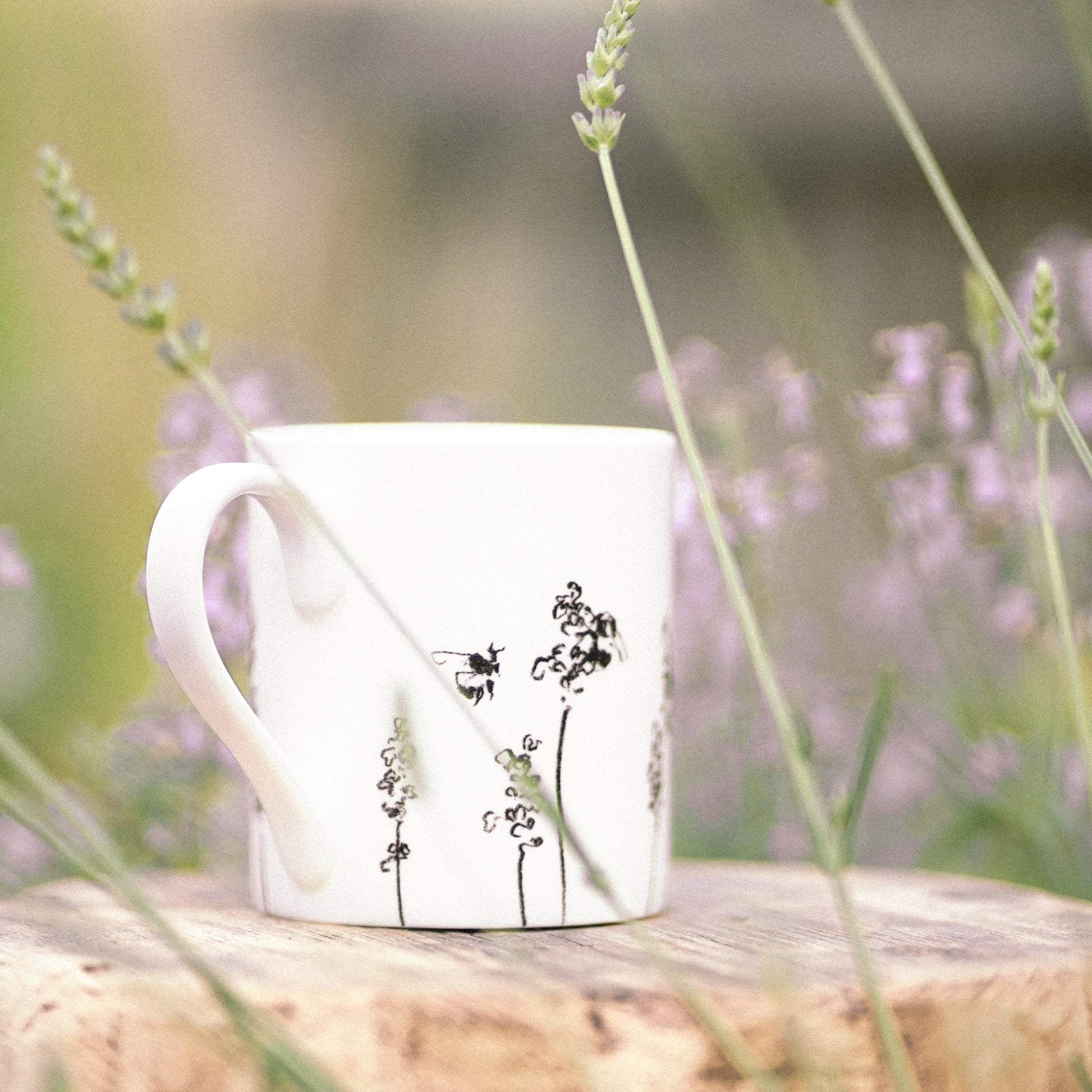 White mug with black floral design on a wooden block surrounded by lavender flowers