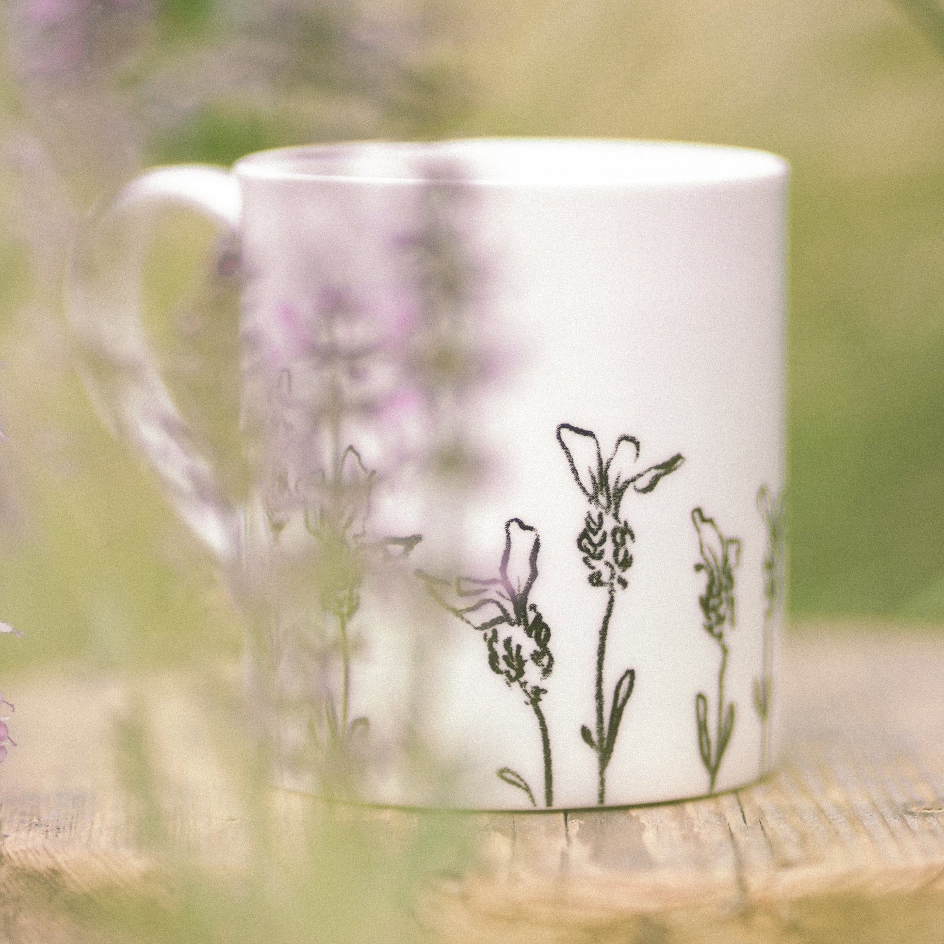 White mug with floral design on a wooden surface surrounded by lavender flowers