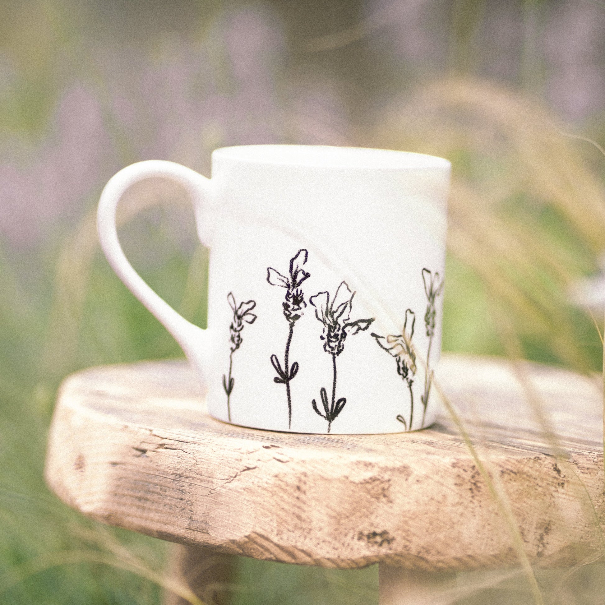 White mug with floral design on a wooden stool in a natural setting