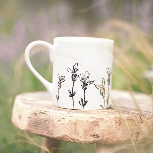 White mug with floral design on a wooden stool in a natural setting