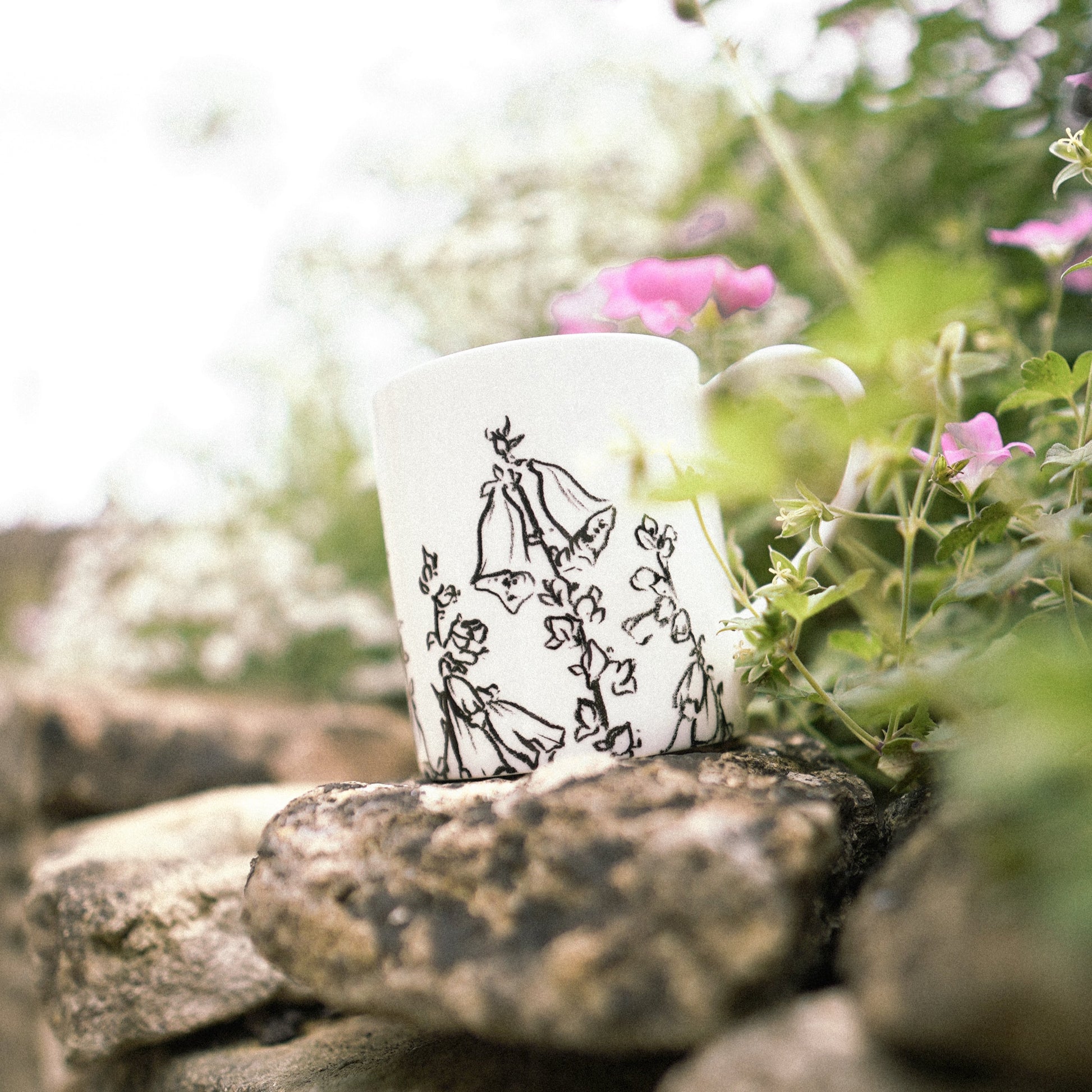 White mug with black illustrations on a rock with a green background.