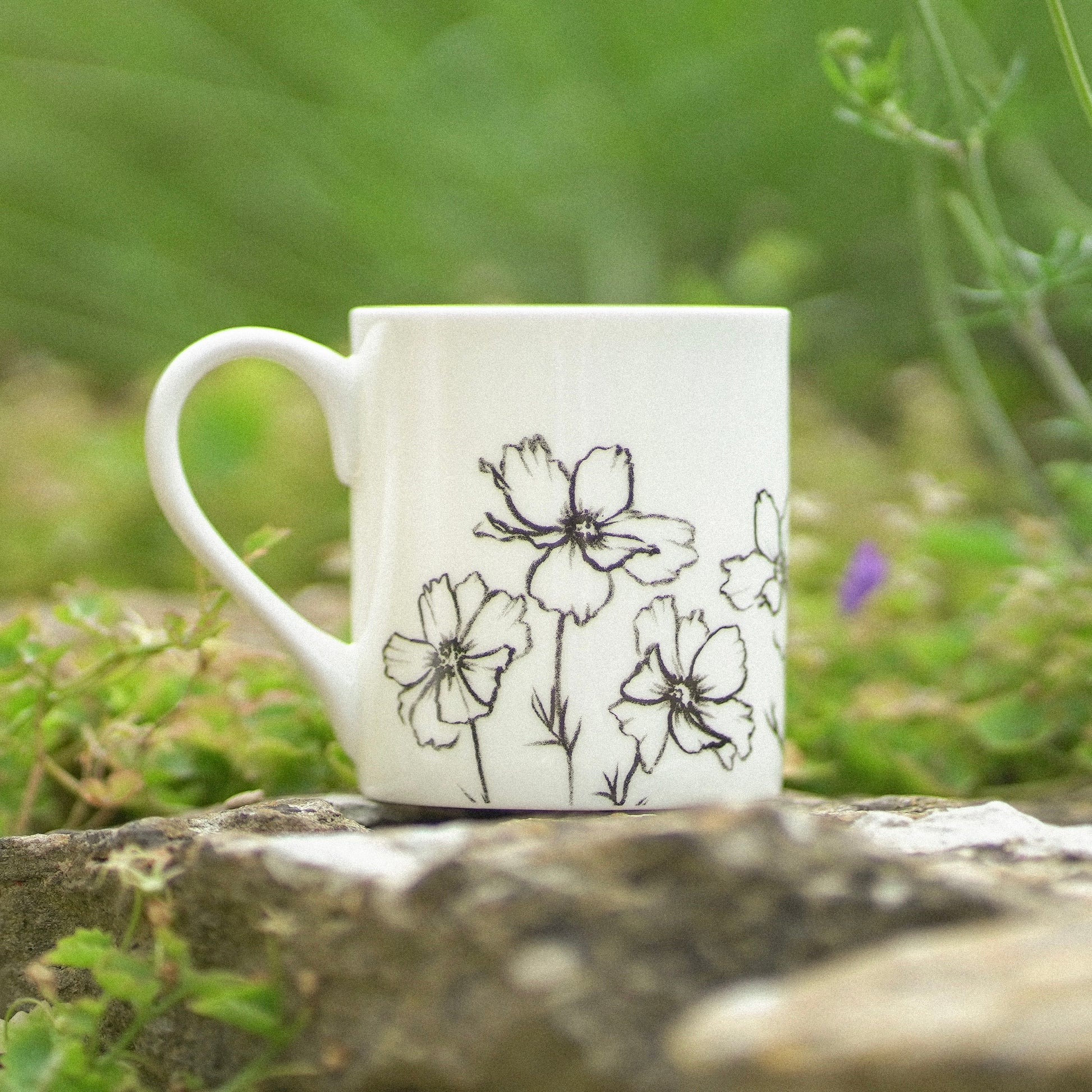 White mug with black floral design on a stone surface with a natural background