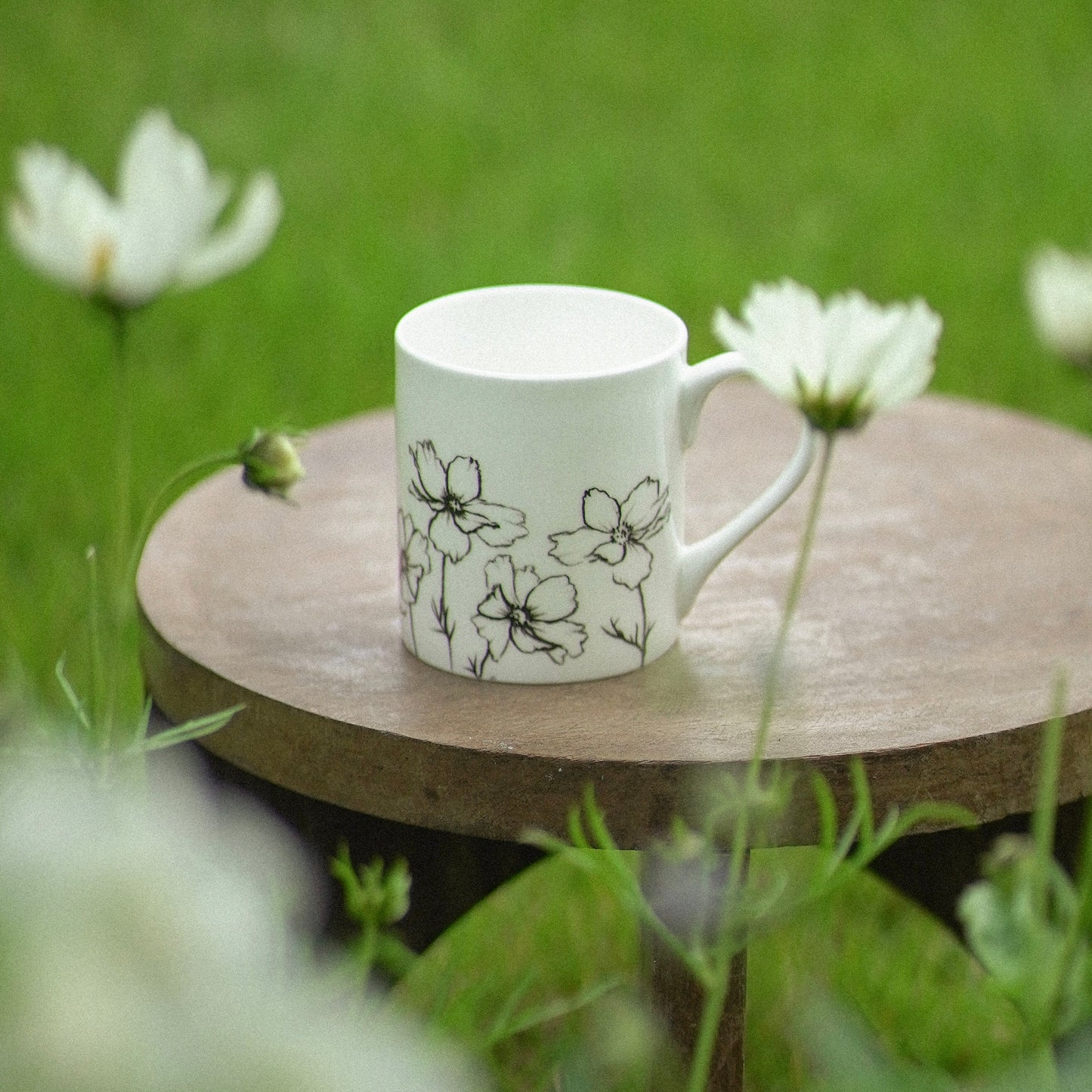 White mug with floral design on a wooden table in a grassy outdoor setting