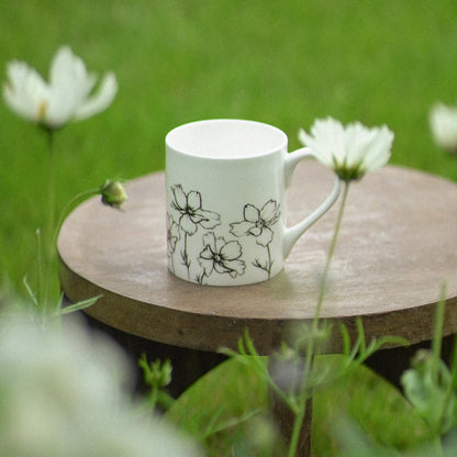 White mug with floral design on a wooden table in a grassy outdoor setting