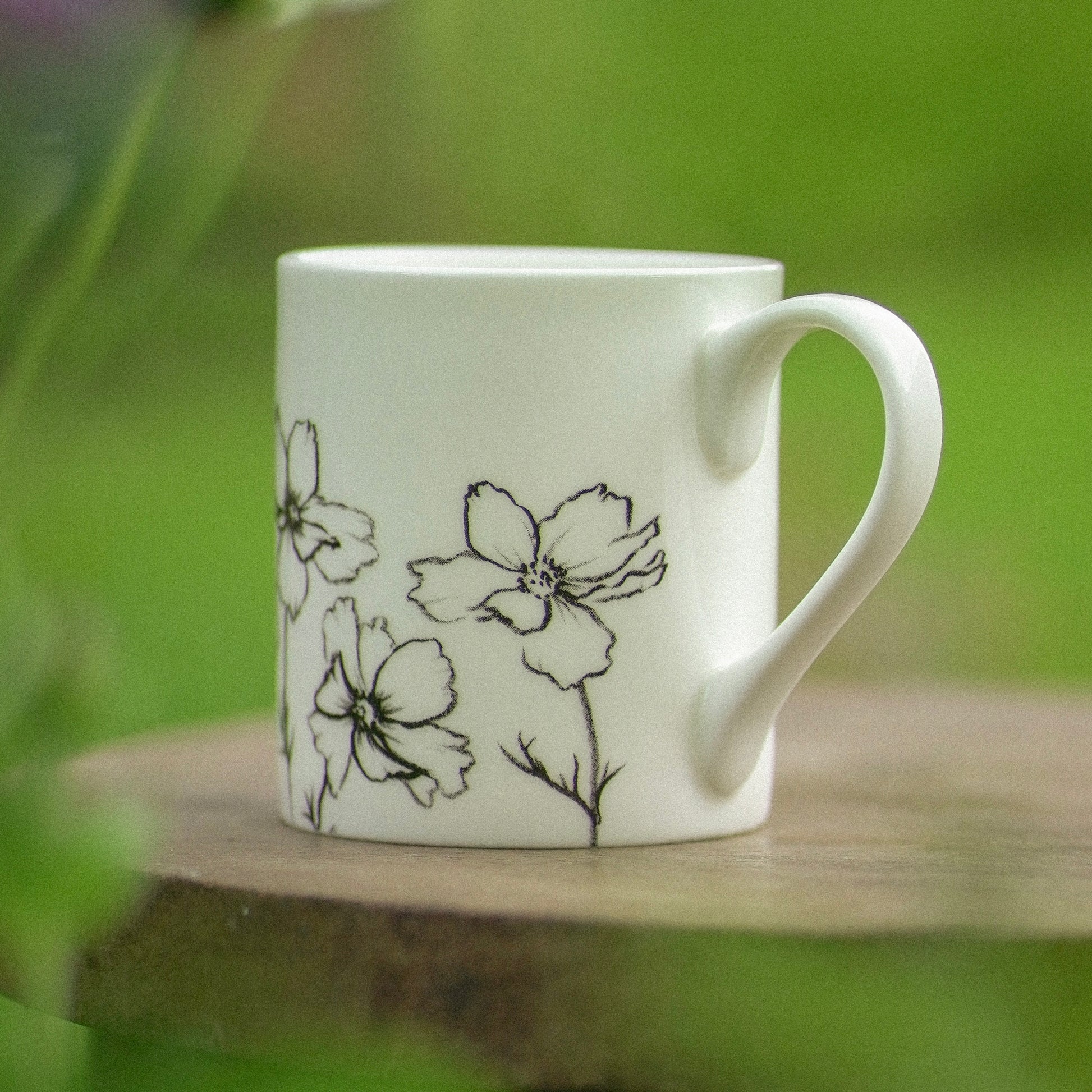 White mug with floral design on a wooden surface with a green blurred background