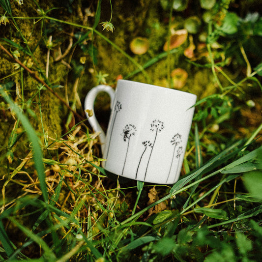 White mug with black floral design on grass