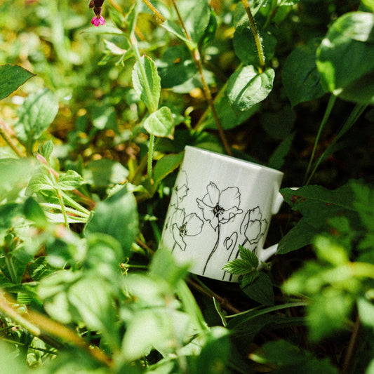 White mug with black floral design placed among green plants