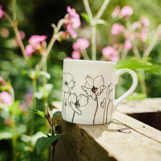 White mug with floral design on a wooden ledge with flowers in the background