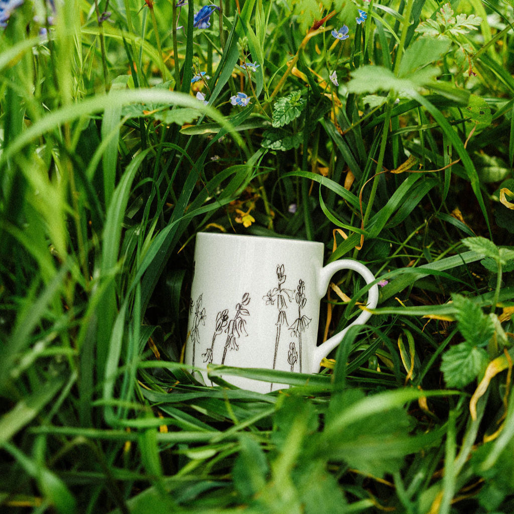 White mug with floral design in a grassy field with blue flowers