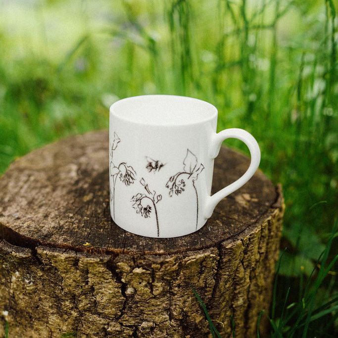 White mug with floral design on a wooden stump in a grassy area