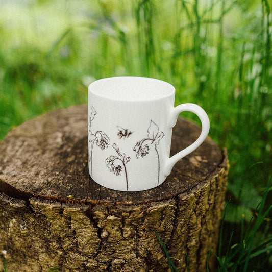 White mug with floral design on a wooden stump in a grassy area
