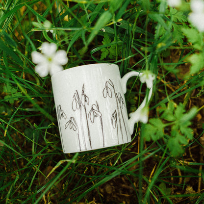 White mug with line drawings of flowers, laid on grassy background