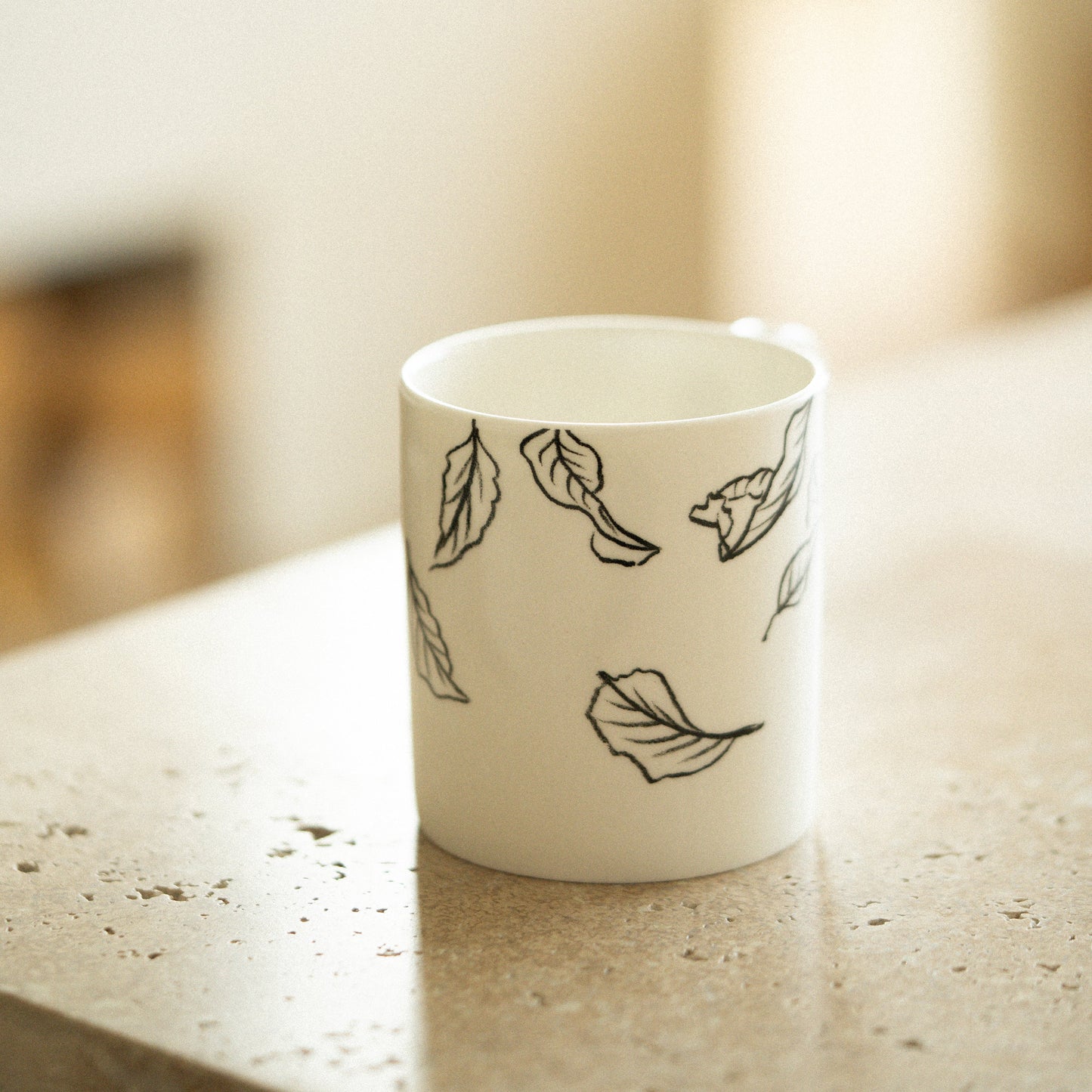 White mug with black leaf patterns on a light surface