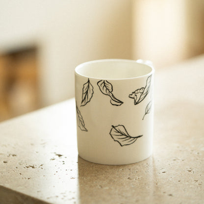 White mug with black leaf patterns on a light surface