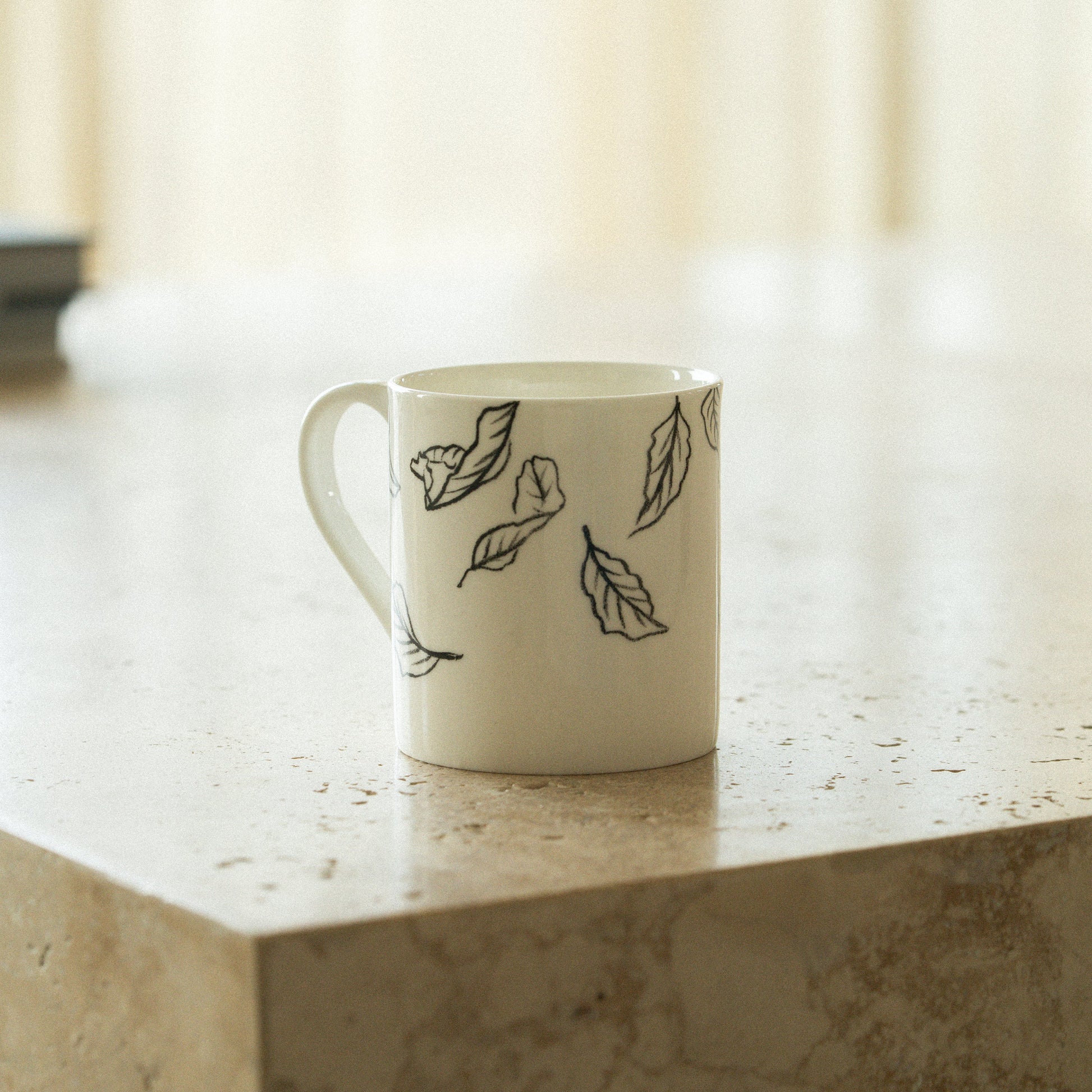 White mug with black leaf patterns on a marble surface