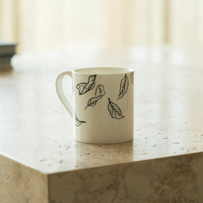 White mug with black leaf patterns on a marble surface