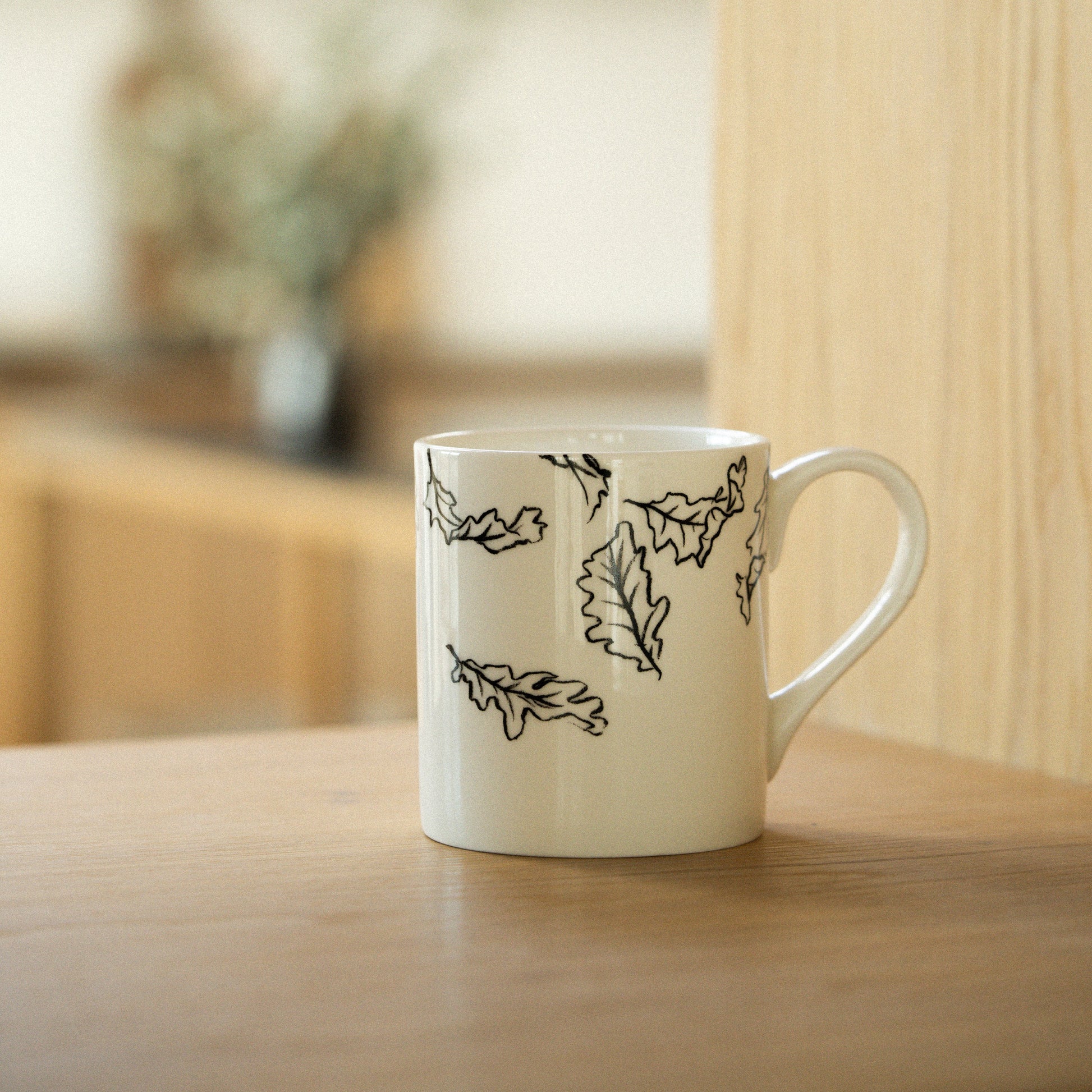 White mug with black leaf patterns on a wooden surface
