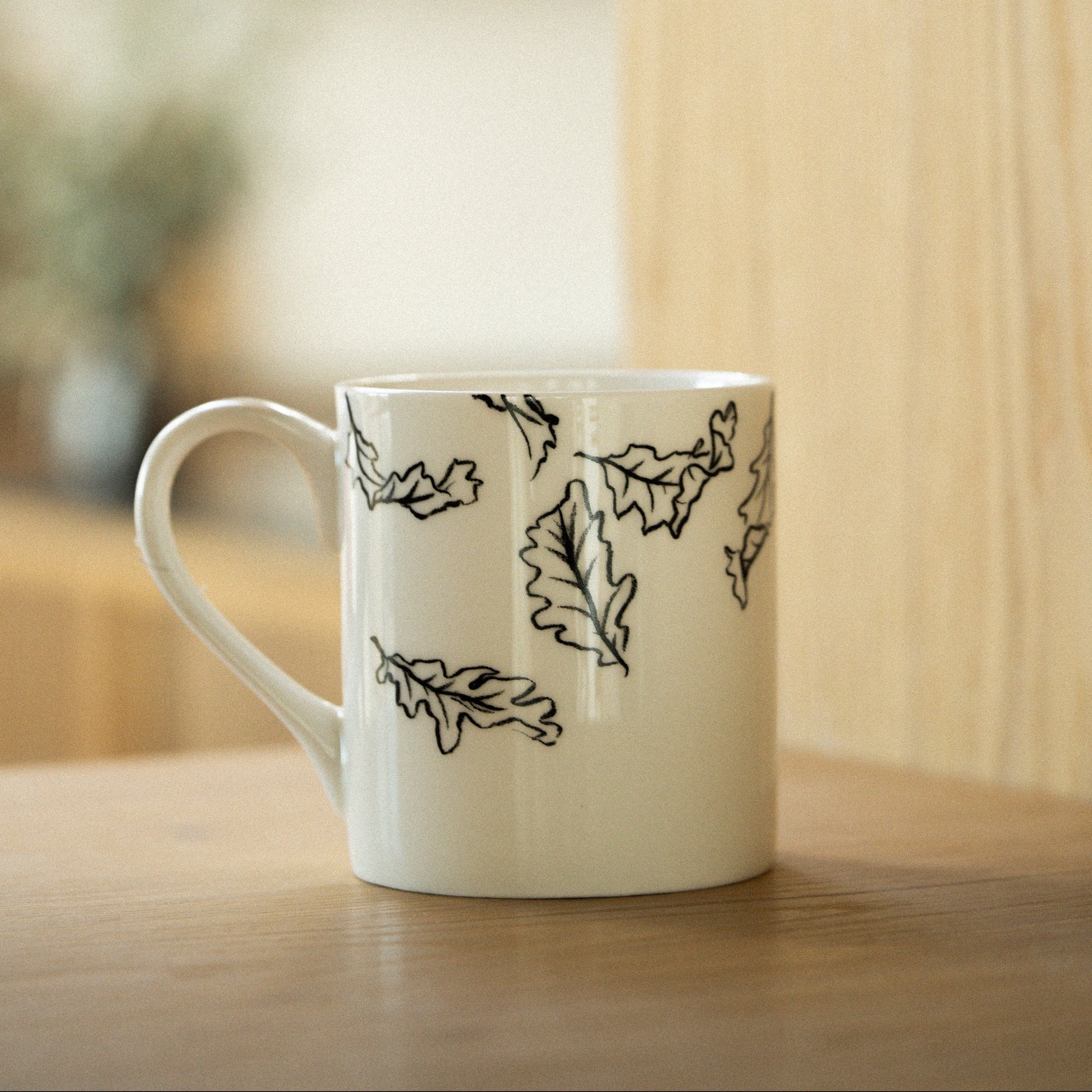 White mug with black leaf patterns on a wooden surface