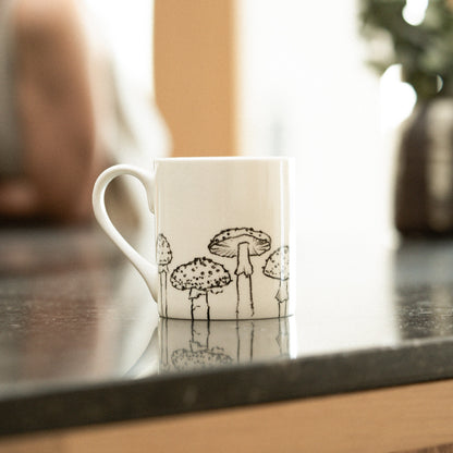 White mug with black mushroom design on a dark surface