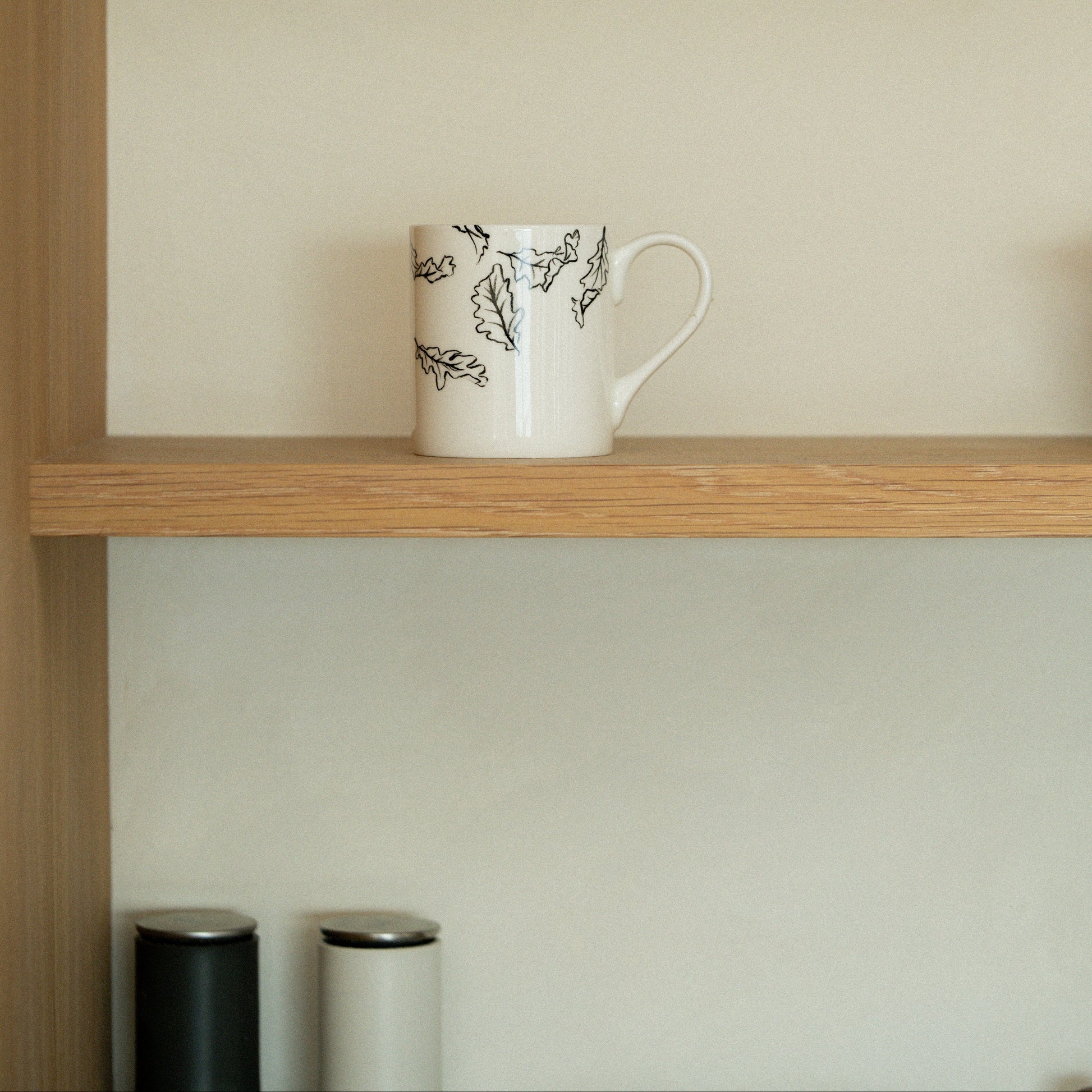 White mug with black design on a wooden shelf against a beige wall.