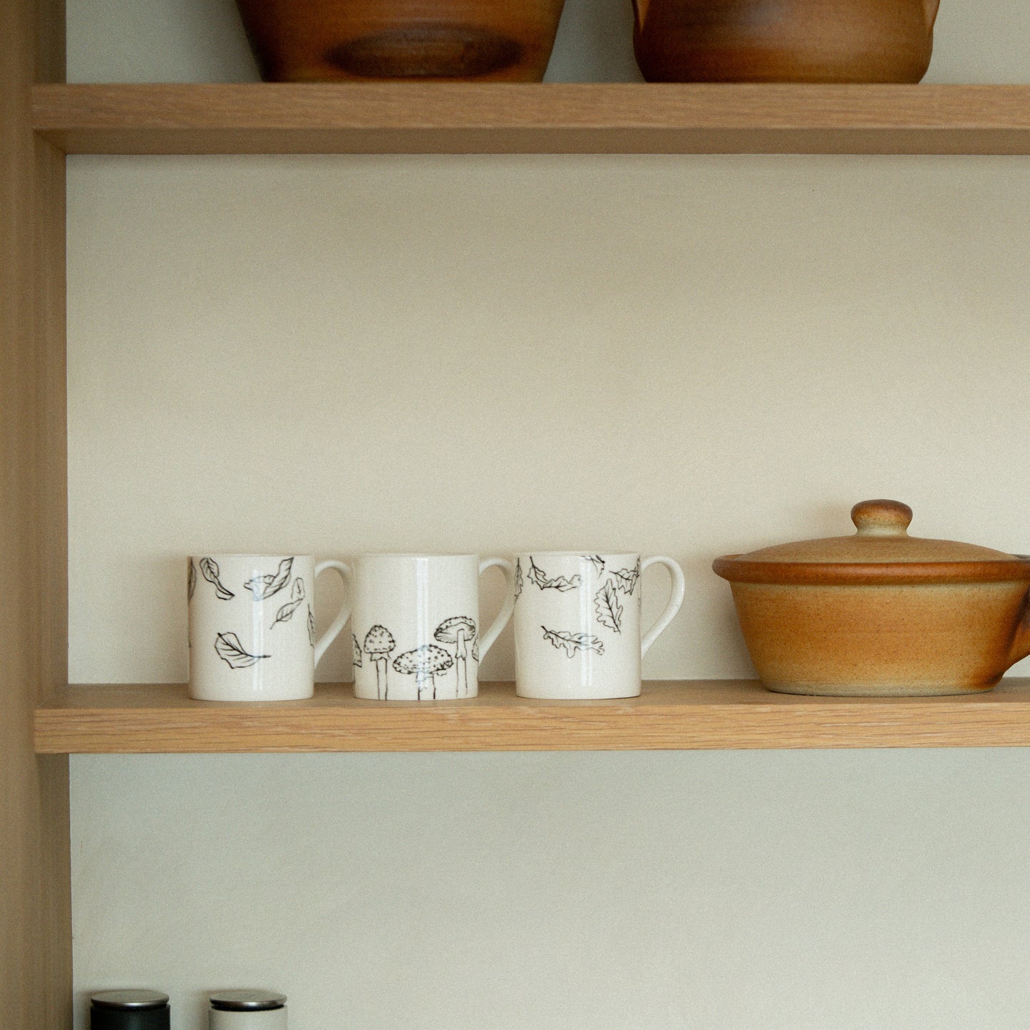 Wooden shelves with ceramic mugs and a pot against a white wall